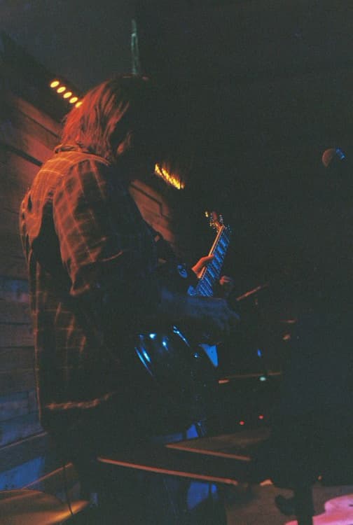 Colby playing electric guitar on a dark stage, lit red and blue